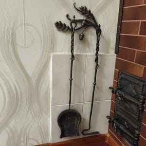 Peut inclure: Un ensemble d'outils de chemin&eacute;e en fer forg&eacute;, comprenant une pelle et un tisonnier. L'ensemble est brun fonc&eacute; avec des accents d&eacute;coratifs de feuilles et de glands. Les outils sont suspendus &agrave; un support mural assorti.