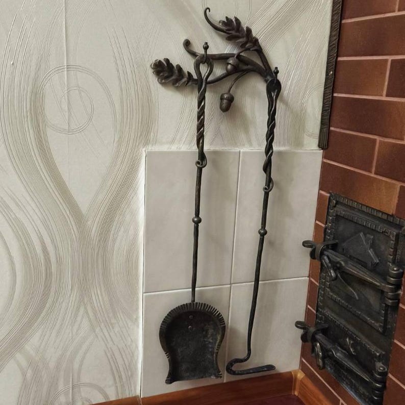 Peut inclure: Un ensemble d'outils de chemin&eacute;e en fer forg&eacute;, comprenant une pelle et un tisonnier. L'ensemble est brun fonc&eacute; avec des accents d&eacute;coratifs de feuilles et de glands. Les outils sont suspendus &agrave; un support mural assorti.