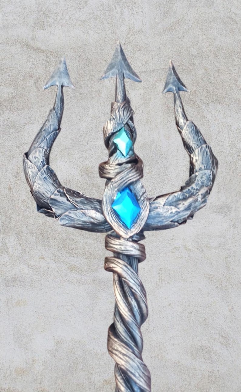 May include: A silver-colored trident with a twisted handle and two blue gemstones. The trident is made of metal and has a rustic, weathered look.