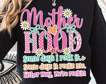 May include: Black sweatshirt with the text "Motherhood" in pink, decorated with daisies and bows. The word "HOOD" is in a checkered pattern. Below, the text reads "Some days I rock it. Some days it rocks me. Either way, We're rockin".