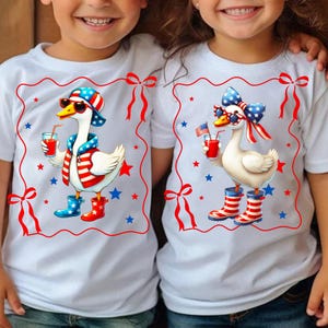 May include: Two white t-shirts with a red border and bow design. Each shirt features a cartoon goose wearing sunglasses, a patriotic hat, and boots, holding a drink with a straw. The goose is decorated with red, white, and blue stars and stripes.