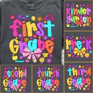 May include: Dark grey crew neck sweatshirt featuring the words "First Grade" in vibrant colours, with accompanying graphics. Additional designs for Kindergarten, Pre-K, Second, Third, and Fourth Grade are also shown. Designs include flowers, bows, pencils, and scissors.