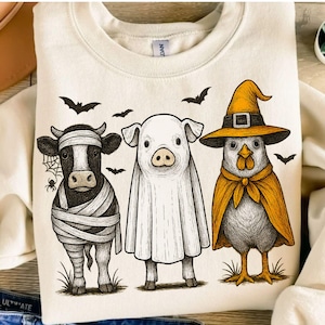 May include: Cream-coloured sweatshirt with a Halloween graphic. The design shows a cow as a mummy, a pig as a ghost, and a chicken in a witch costume, with bats overhead. The graphic is in black and white.