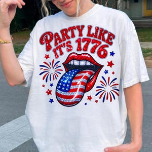 May include: White t-shirt with a graphic design featuring red lips, a tongue with a US flag design, and the text "PARTY LIKE IT'S 1776" in red. The design includes red and blue stars and fireworks.