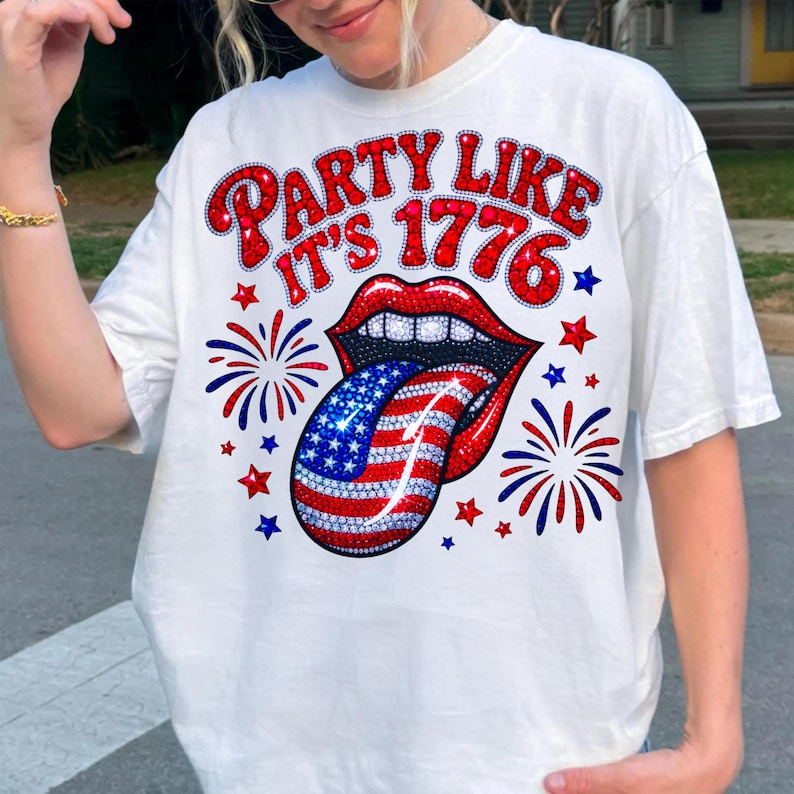 May include: White t-shirt with a graphic design featuring red lips, a tongue with a US flag design, and the text "PARTY LIKE IT'S 1776" in red. The design includes red and blue stars and fireworks.