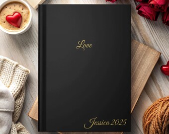 May include: A black journal with the word "Love" in gold script at the top and "Jessica 2025" at the bottom. The journal is on a wooden surface with a cup of coffee with a heart, roses, and a knitted item.