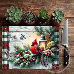 May include: A rectangular glass cutting board with a Christmas theme. It features a red cardinal bird perched on a snowy branch with berries, a lantern, and a plaid border. A stainless steel knife is on the right.
