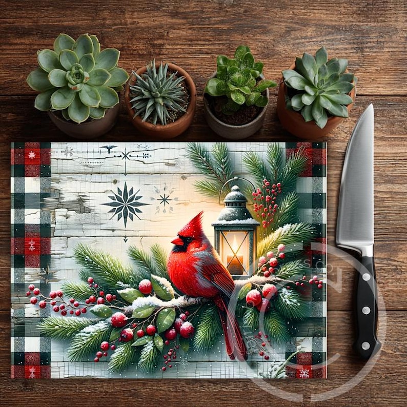 May include: A rectangular glass cutting board with a Christmas theme. It features a red cardinal bird perched on a snowy branch with berries, a lantern, and a plaid border. A stainless steel knife is on the right.
