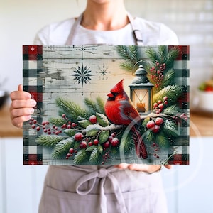 May include: A rectangular decorative piece featuring a vibrant red cardinal perched on a snow-covered branch with red berries and evergreen boughs. A lit lantern and snowflake designs are also present. The border has a black and red plaid pattern.