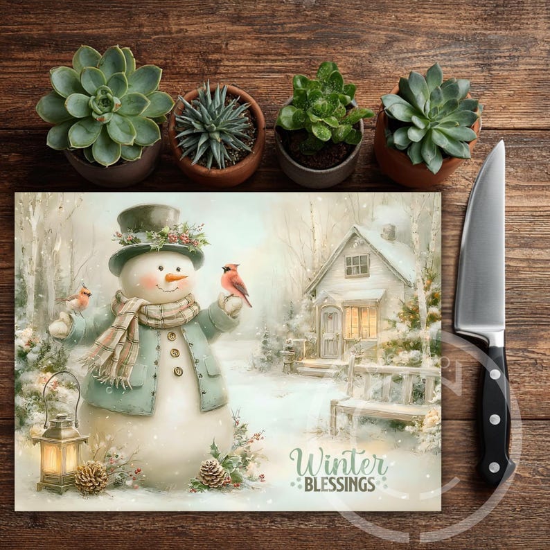 May include: A decorative cutting board with a winter scene featuring a snowman, cardinals, and a snow-covered house. The board has the text "Winter Blessings". A stainless steel knife and potted succulents are also in the image.