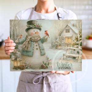 May include: A winter-themed print featuring a snowman wearing a top hat, scarf, and coat, holding a bird. A lantern and a small house are also depicted in a snowy landscape. The text "Winter Blessings" is displayed on the print.