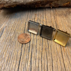 May include: Three square cufflinks in silver, black, and gold, displayed on a rustic wooden surface. A US penny is next to the cufflinks for size comparison. The cufflinks have a rectangular design.