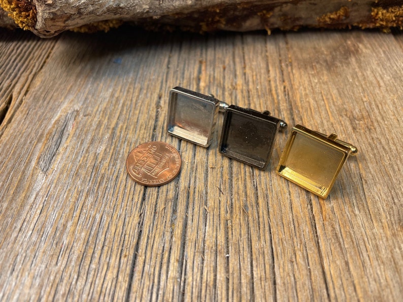 May include: Three square cufflinks in silver, black, and gold, displayed on a rustic wooden surface. A US penny is next to the cufflinks for size comparison. The cufflinks have a rectangular design.