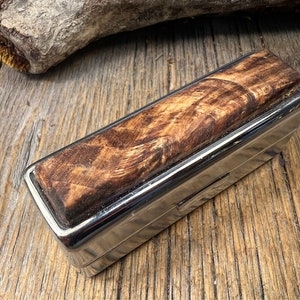 May include: A small, rectangular, silver metal box with a wooden lid. The lid has a natural wood grain pattern with brown and tan tones.