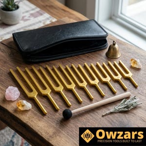 May include: A collection of gold-colored tuning forks, a black zippered case, a small bell, crystals, a wooden mallet with a black head, and dried herbs are arranged on a wooden surface. The image includes the text "Owzars PRECISION TOOLS BUILT TO LAST".