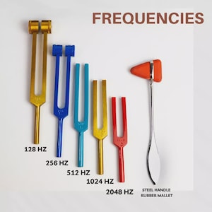 May include: A collection of tuning forks in various colors, including gold, blue, and red, with the text "FREQUENCIES" at the top. Each fork is labeled with its frequency in Hertz, ranging from 128 Hz to 2048 Hz. A steel handle rubber mallet is also present.