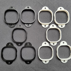 May include: Eight plastic frames, four black and four white, with a square opening in the centre. The frames are designed to hold small objects, such as photos or artwork.