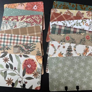 Könnte beinhalten: Eine Sammlung dekorativer Karteikarten mit verschiedenen Mustern. Designs umfassen florale, karierte und winterliche Illustrationen. Farben sind Rot, Grün, Braun und Gold. Jede Karte hat unten einen Schlitz zur Verwendung in einer Kartei.