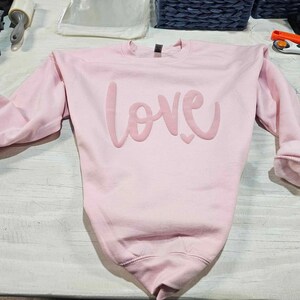 May include: A pink sweatshirt with the word "LOVE" printed in a large, stylized font.