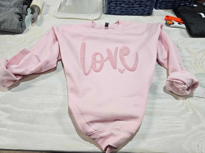 May include: A pink sweatshirt with the word "LOVE" printed in a large, stylized font.