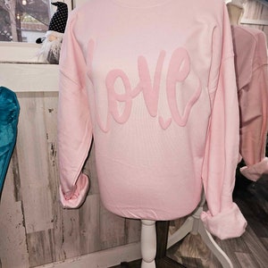 May include: A pink sweatshirt with the word "LOVE" in a large, pink, cursive font.