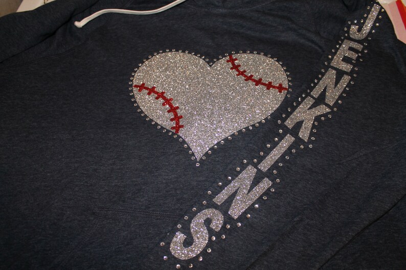 May include: A dark blue hoodie with a silver glitter baseball heart and the word "SKINZ" in silver glitter on the sleeve.