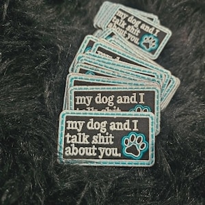 May include: A stack of rectangular embroidered patches with a black background and light blue border. The text reads "my dog and I talk shit about you." in white lettering, accompanied by a light blue embroidered paw print graphic on the right.