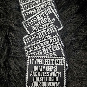 May include: A stack of rectangular black embroidered patches with a white rope-style border. Each patch features the white text: I TYPED BITCH IN MY GPS AND GUESS WHAT? I'M SITTING IN YOUR DRIVEWAY. The patches are arranged in a cascading vertical pile.