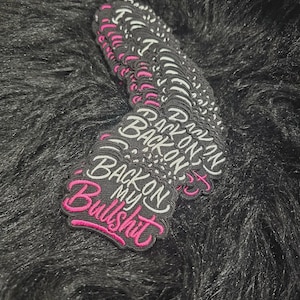 May include: A stack of embroidered patches with a black background. The text reads "BACK ON MY Bullshit" in white and pink thread. The word "BACK" and "ON" are in white, "MY" is in white, and "Bullshit" is in a cursive pink font.