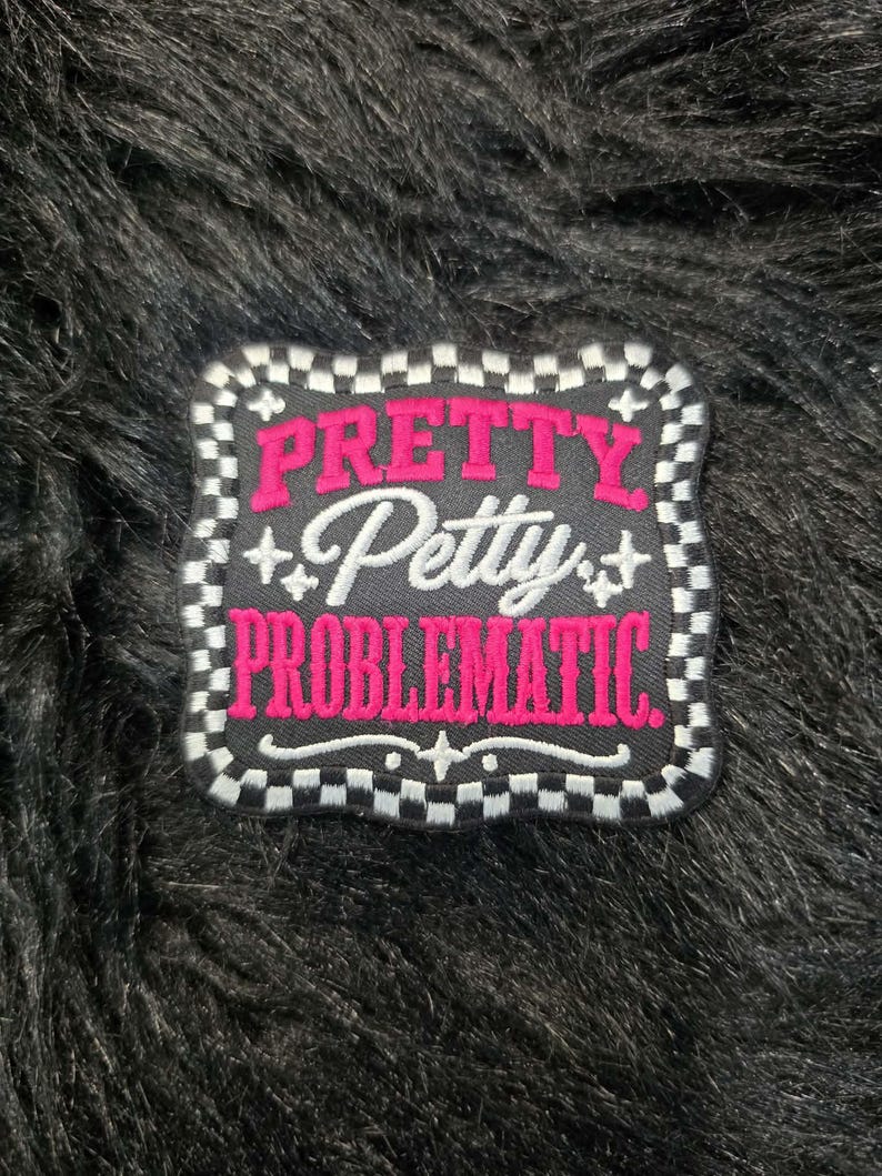 May include: A square embroidered patch with rounded corners featuring a black background and a white and black checkered border. The text PRETTY in pink, Petty in white script, and PROBLEMATIC in pink is centered with small white star accents.