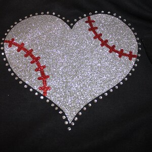 May include: A silver glitter heart with a red baseball stitch design. The heart is outlined with silver rhinestones.