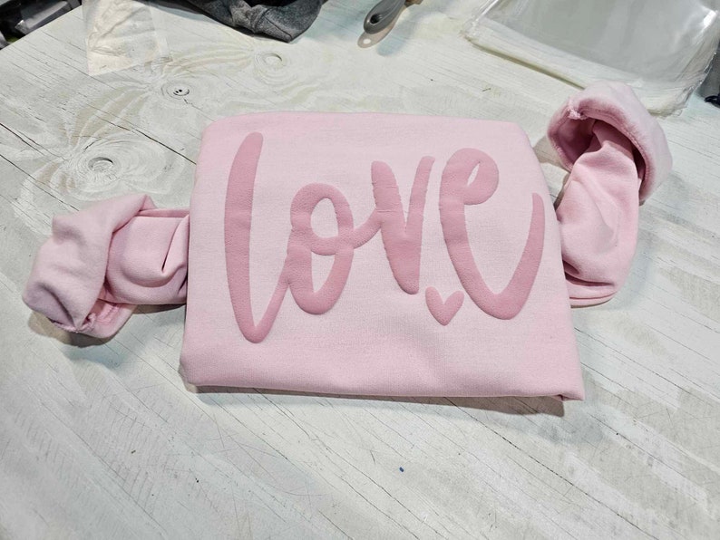 May include: Pink sweatshirt with the word "LOVE" in a pink, cursive font.