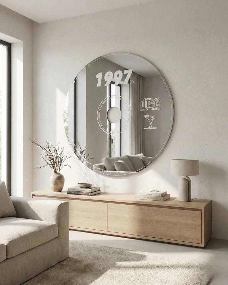 May include: A large, round mirror designed to resemble a CD, mounted on a wall. The mirror features the year "1997" and the words "Compact Disc Digital Audio" with a palm tree graphic. The mirror reflects a living room with a sofa and wooden furniture.