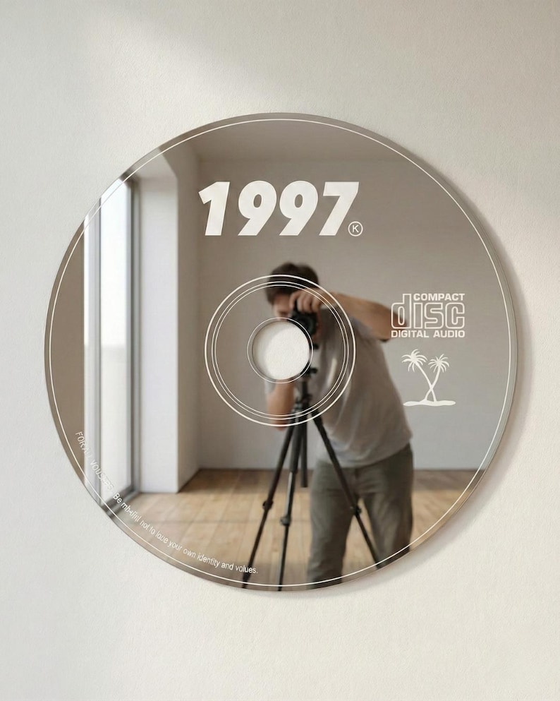 May include: A reflective CD-shaped mirror with the year "1997" printed on it. The mirror reflects a person with a camera on a tripod. The words "COMPACT DISC DIGITAL AUDIO" and two palm trees are also visible.