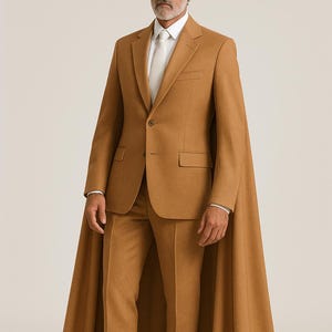 May include: A tan suit with a matching cape. The suit includes a blazer, trousers, and a white dress shirt with a light-colored tie. The model is wearing white boots. The suit is a solid color and has a classic design.