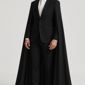 May include: A formal black suit with a matching cape. The suit includes a blazer, trousers, and a white dress shirt with a tie. The cape extends to the ankles. The person is wearing white leather boots.
