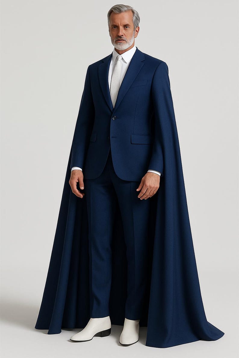 May include: A navy blue suit with a matching cape. The suit includes a blazer, trousers, and a white dress shirt with a tie. The model is wearing white boots. The cape extends to the ankles.