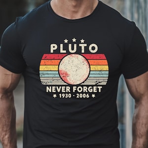 May include: Black t-shirt with a vintage-style graphic of Pluto, a planet with a red, white, and blue color scheme. The text "Pluto Never Forget 1930 - 2006" is printed on the shirt.
