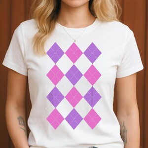 Puede incluir: Camiseta blanca con un patrón de rombos repetido en tonos rosa y morado. El diseño de rombos está compuesto por formas de diamante con un patrón de cruces punteadas en el centro de cada diamante. La camiseta tiene mangas cortas y cuello redondo.