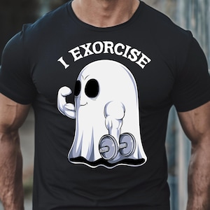 May include: Black t-shirt featuring a cartoon ghost lifting weights. The ghost has large black eyes and is flexing its arm. Above the ghost, the text reads "I EXORCISE" in white, arched lettering. The design is a humorous take on fitness.