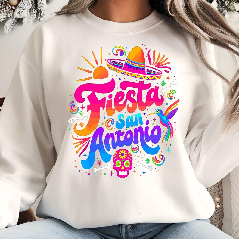 May include: White sweatshirt with a colorful graphic design featuring the text "Fiesta San Antonio" with a sombrero, a hummingbird, and a sugar skull.