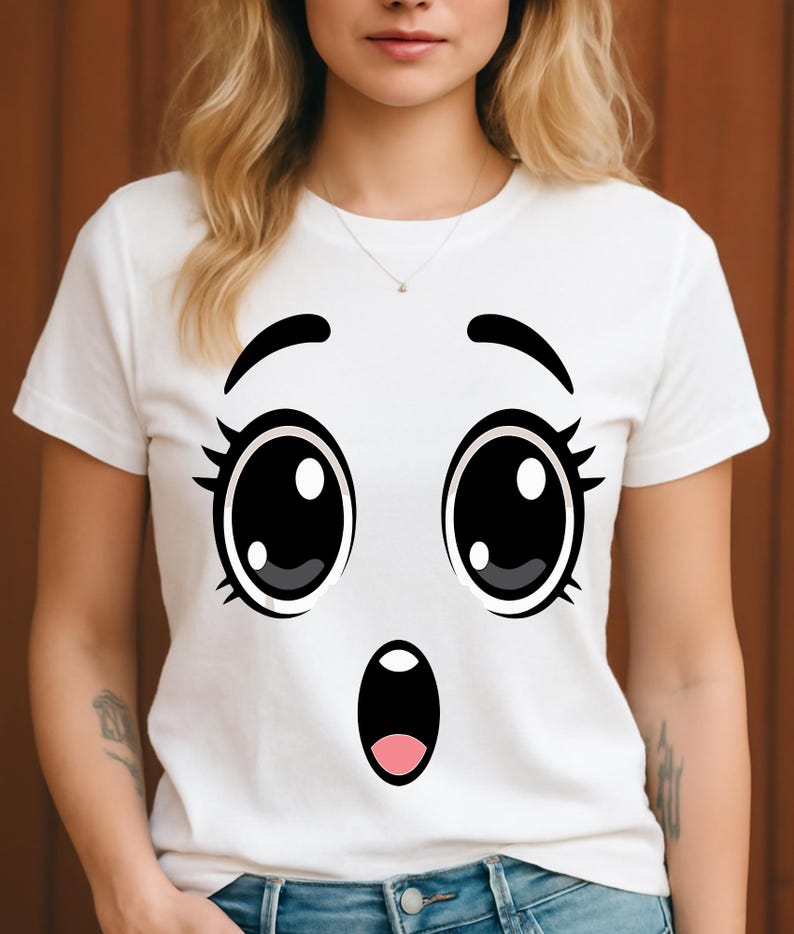 Puede incluir: Camiseta blanca con un dise&ntilde;o de cara de dibujos animados sorprendida. El gr&aacute;fico incluye ojos negros grandes con reflejos blancos, pesta&ntilde;as negras y una boca abierta sorprendida con el interior rosa. La camiseta la lleva una persona.