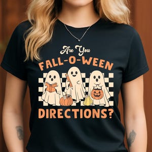 Könnte beinhalten: Schwarzes T-Shirt mit dem Text "Are You FALL-O-WEEN DIRECTIONS?" mit drei Cartoon-Geistern. Die Geister halten ein Buch, einen Bleistift und einen Kürbis. Das Design enthält orange und weiße Farben.