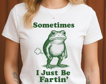 May include: White t-shirt with a green illustration of a frog and the text "Sometimes I Just Be Fartin'". The frog is drawn in a vintage style, with a cloud graphic indicating a fart.