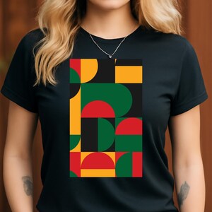 May include: Black t-shirt featuring a geometric design with red, green, yellow, and black shapes. The design includes semi-circles and rectangles arranged in a vertical pattern. The shirt has short sleeves and a crew neck.