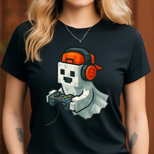 May include: Black t-shirt featuring a pixelated ghost character wearing an orange cap and headphones, holding a video game controller. The ghost has a white body and is playing a video game. The design is a fun, gamer-themed graphic.