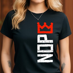 May include: Black t-shirt featuring a red crown graphic above the vertical text "NDP" in white. The t-shirt has short sleeves and a crew neck. The design is printed on the front of the shirt.
