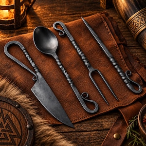 May include: A set of four hand-forged metal utensils including a knife, a spoon, a two-pronged fork, and a pointed skewer. Each piece features a dark, matte finish with a twisted handle design and a decorative curled loop at the end of the handle.