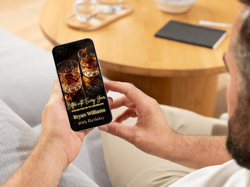 Peut inclure: Un smartphone affiche une invitation num&eacute;rique pour le 40e anniversaire de Bryan Williams. L'invitation pr&eacute;sente deux verres de liquide ambr&eacute;, probablement du whisky, avec un design or et noir. Le texte dit "Better with Every Year."