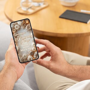 May include: A smartphone displays a Friendsgiving dinner invitation. The design features white and gold pumpkins, leaves, and text. The invitation includes the words "Friendsgiving Dinner" and the names "Mia & Alex."